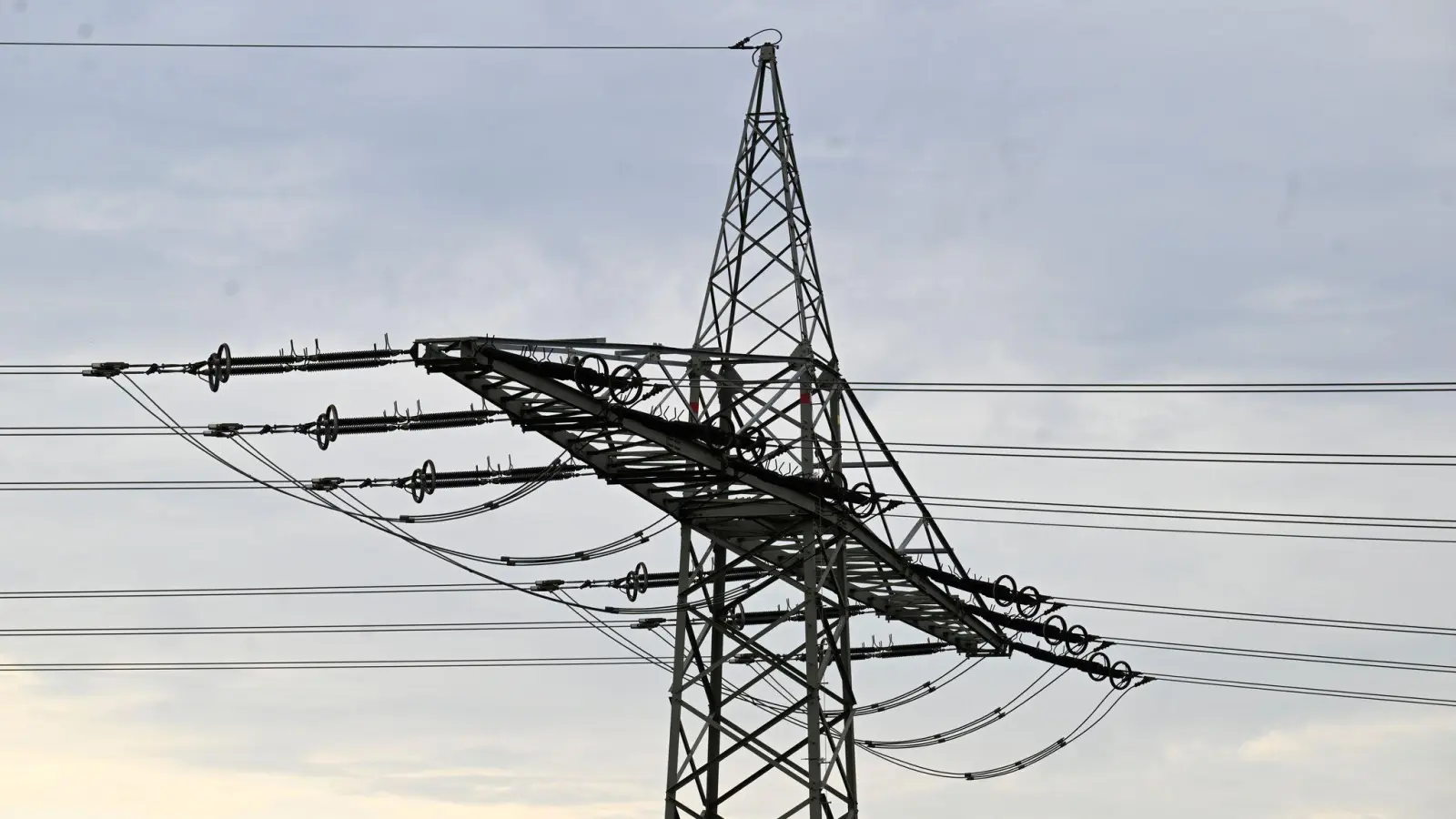 Ein Strommast steht vor grauen Wolken. In einigen Teilen von Luhe-Wildenau ist am Donnerstagmorgen der Strom ausgefallen. (Symbolbild: Roberto Pfeil/dpa)