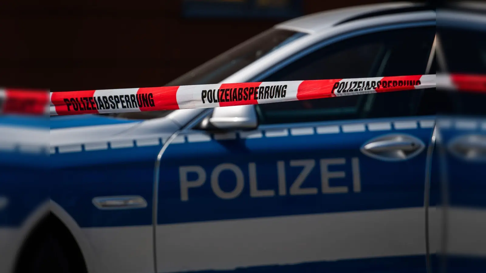 Ein Polizeiauto steht hinter einem Absperrband der Polizei. (Symbolbild: Robert Michael/dpa)