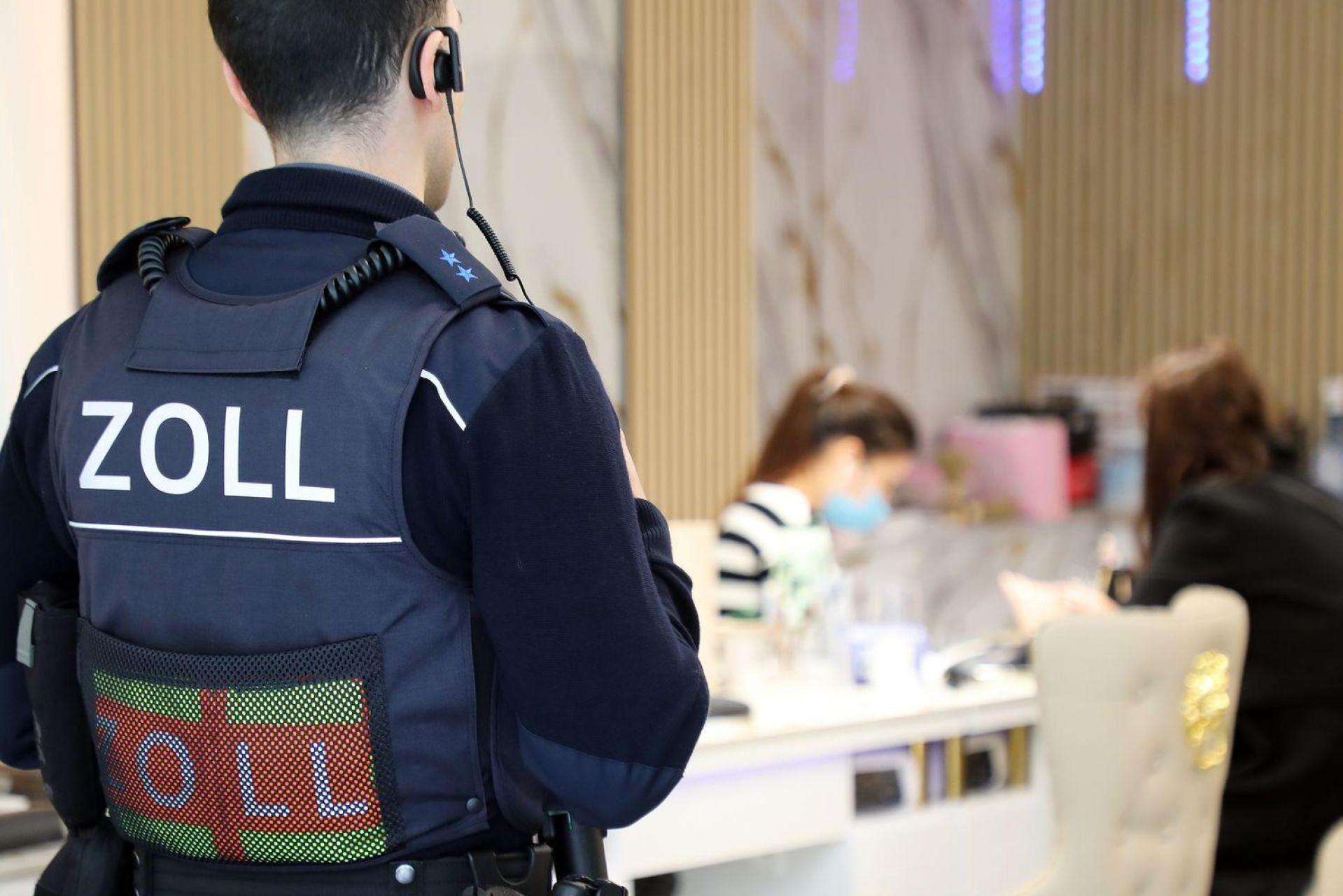 Ein Zollbeamter steht bei einer Kontrolle in Köln in der Tür eines Nagelstudios. Im Landkreis Neustadt/WN haben Zöllner einen umfangreichen Fall von Schwarzarbeit, Mindestlohnverstößen und illegaler Beschäftigung in zwei Nagelstudios aufgedeckt. (Symbolbild: -/dpa)