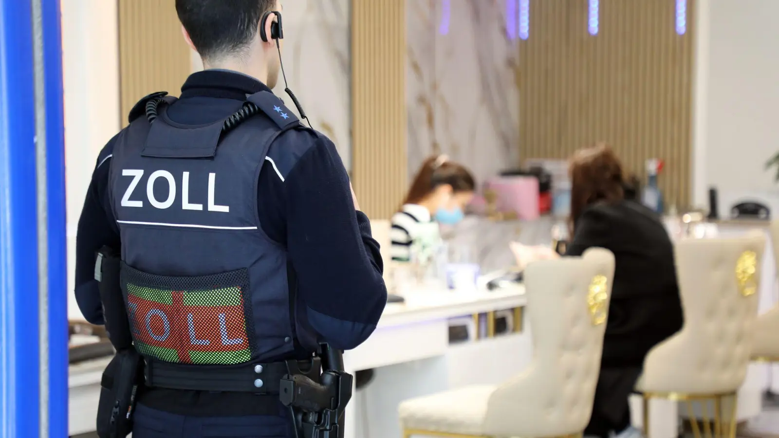 Ein Zollbeamter steht bei einer Kontrolle in Köln in der Tür eines Nagelstudios. Im Landkreis Neustadt/WN haben Zöllner einen umfangreichen Fall von Schwarzarbeit, Mindestlohnverstößen und illegaler Beschäftigung in zwei Nagelstudios aufgedeckt. (Symbolbild: -/dpa)