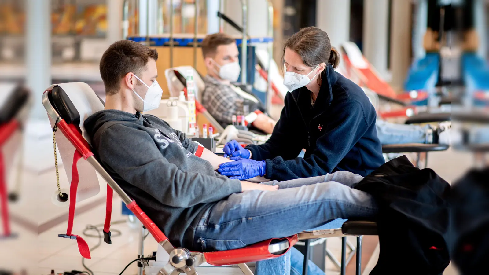 Eine Mitarbeiterin beim Blutspendedienst des Deutschen Roten Kreuzes (DRK) nimmt von einem Spender Blut ab.  (Symbolbild: Hauke-Christian Dittrich/dpa)