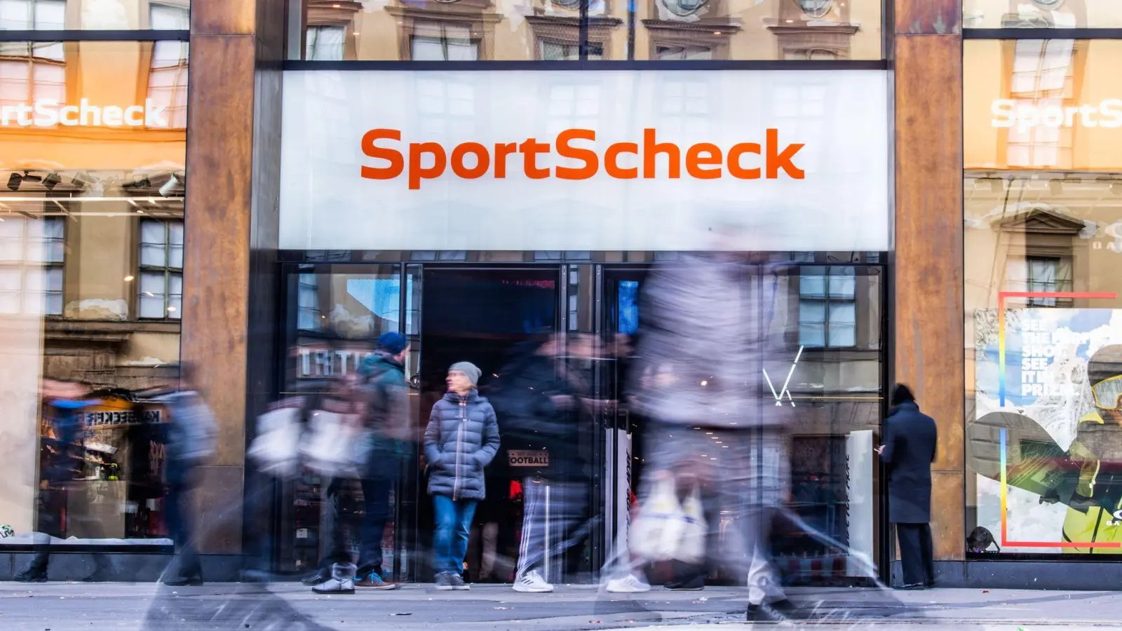 Personen gehen an einer Sportscheck-Filiale in der Münchener Fußgängerzone vorbei. (Bild: Lino Mirgeler/dpa)