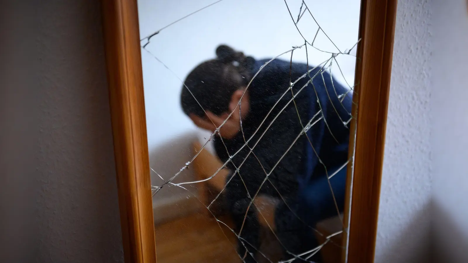 Eine Frau sitzt neben einem gesprungenen Spiegel auf einem Bett und hält ihren Kopf in den Händen. (Symbolbild: Jonas Walzberg/dpa)