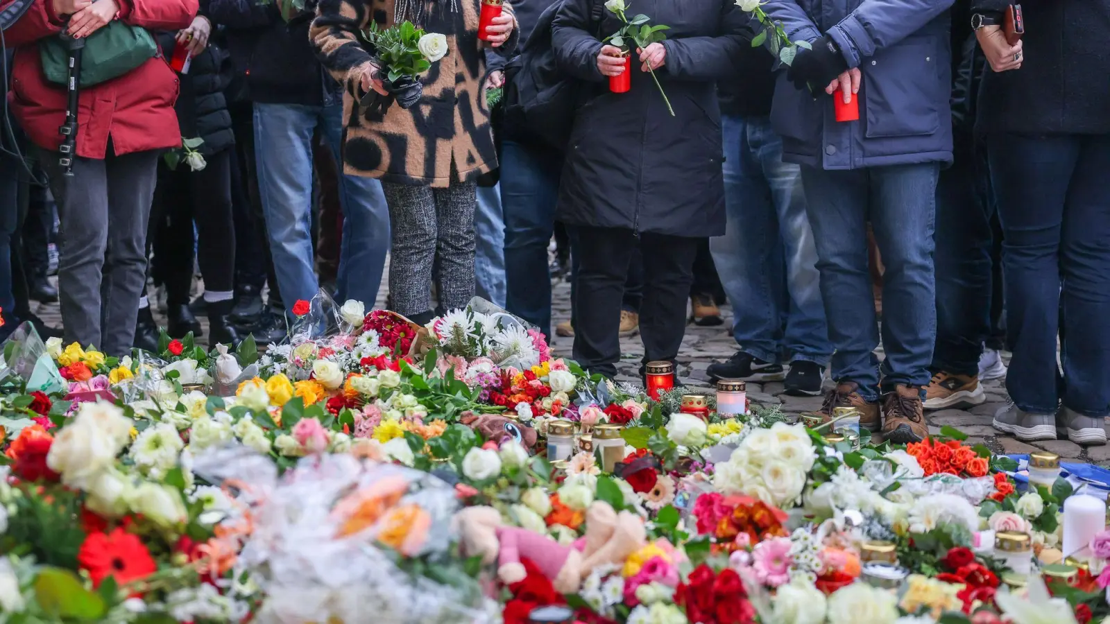 Menschen legen Blumen und Kerzen am offiziellen Gedenkort nach Todesfahrt auf Weihnachtsmarkt in Magdeburg an der Johanniskirche nieder. Am Vorabend war ein Autofahrer auf dem Magdeburger Weihnachtsmarkt in eine Menschengruppe gefahren. Es gab mehrere Tote und Verletzte. (Bild: Jan Woitas/dpa)