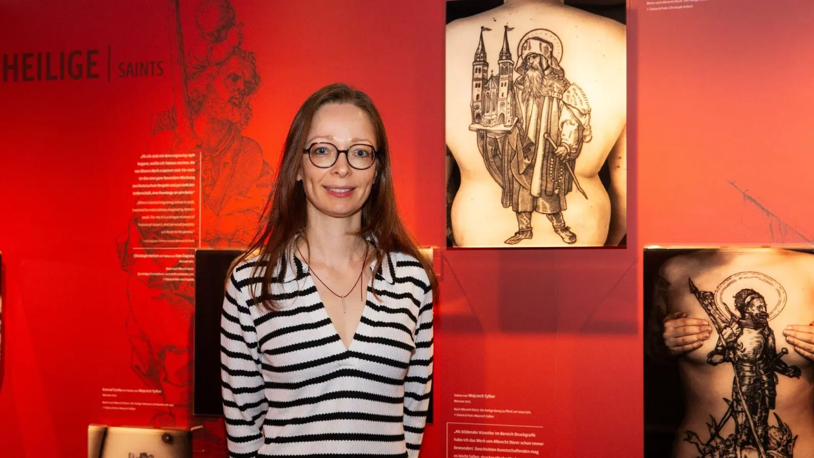 Die Museumsleiterin und Kuratorin Christine Demele steht vor einer Ausstellungstafel mit Fotografien von Tätowierungen, die nach Kunstwerken von Albrecht Dürer entstanden sind. (Bild: Oliver Frank/Albrecht-Dürer-Haus/dpa)