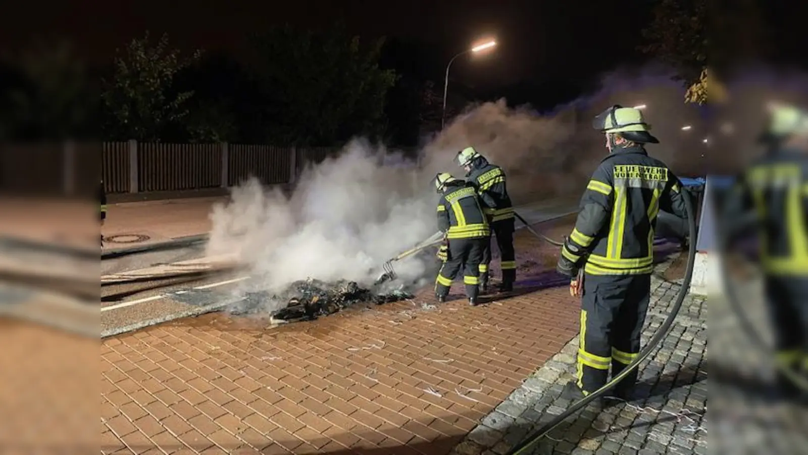 Die zur Abholung bereitgestellten Papiercontainer an der Pfalzgraf-Friedrich-Mittelschule brennen vollständig ab. Auch der Asphalt des Gehsteigs wird in diesem Bereich in Mitleidenschaft gezogen. Die Feuerwehrkräfte können nur mehr Nachlöscharbeiten durchführen.  (Bild: Anton Schwägerl/exb)