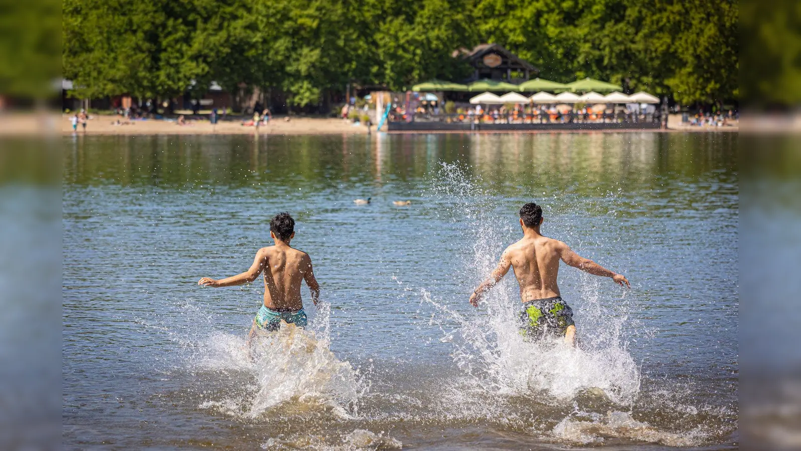 Zwei junge Männer rennen bei sonnigem Wetter in das Wasser eines Sees. (Bild: Moritz Frankenberg/dpa/Symbolbild)